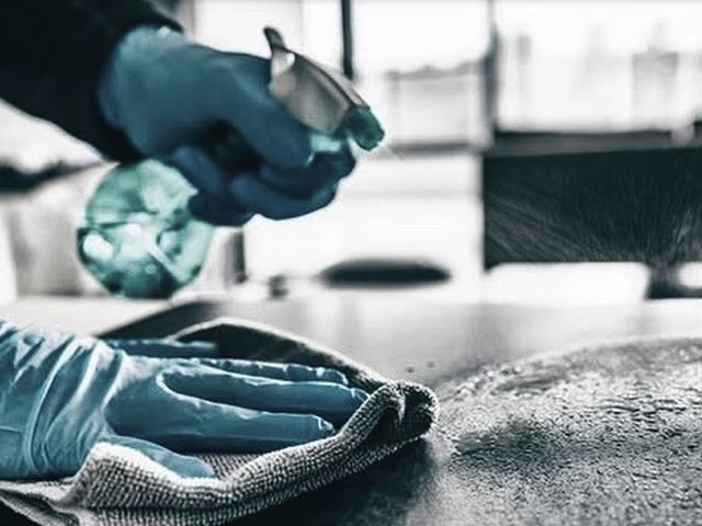 Gloved hands spraying disinfectant and wiping down a hard surface